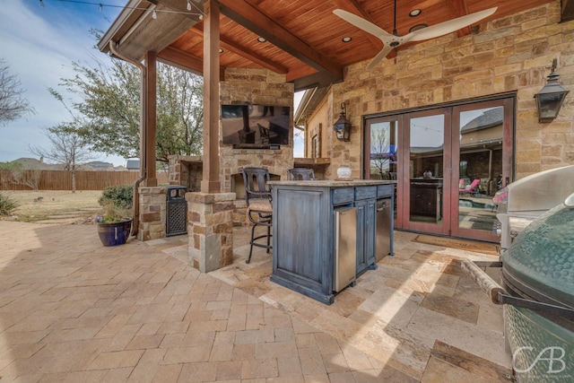 view of patio with an outdoor stone fireplace, a ceiling fan, exterior kitchen, area for grilling, and fence