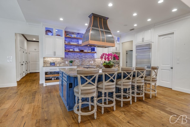 kitchen with stainless steel built in fridge, white cabinetry, crown molding, and island exhaust hood