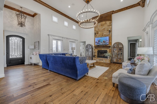 living room featuring crown molding, a fireplace, a towering ceiling, a chandelier, and wood-type flooring