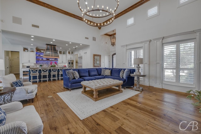 living area featuring a towering ceiling, ornamental molding, a chandelier, light wood-style floors, and visible vents