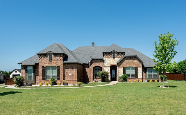 french provincial home featuring fence, a shingled roof, a front lawn, and brick siding
