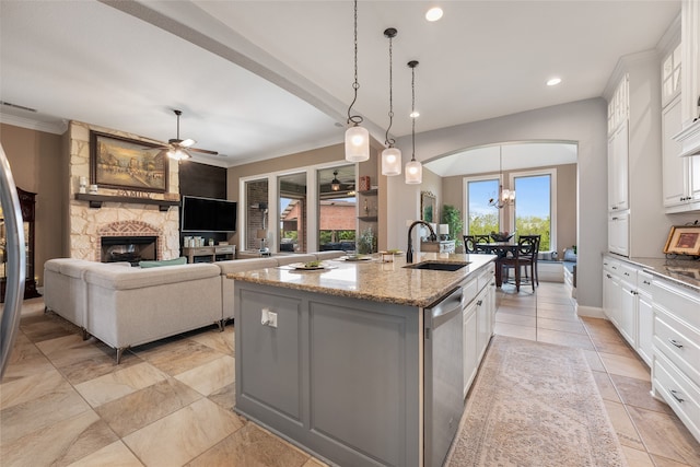 kitchen featuring a sink, a fireplace, a kitchen island with sink, ceiling fan with notable chandelier, and stainless steel dishwasher