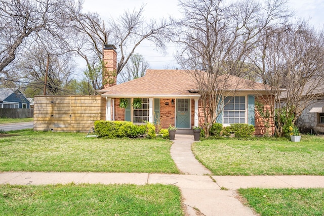 view of front facade featuring a chimney, a shingled roof, brick siding, and a front yard