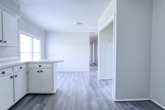 kitchen with light countertops, light wood finished floors, white cabinetry, a peninsula, and baseboards