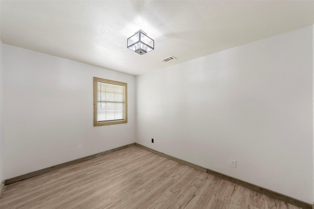 empty room with baseboards, visible vents, light wood-style floors, and a textured ceiling