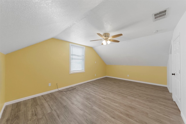 additional living space featuring baseboards, a textured ceiling, light wood-style floors, visible vents, and a ceiling fan