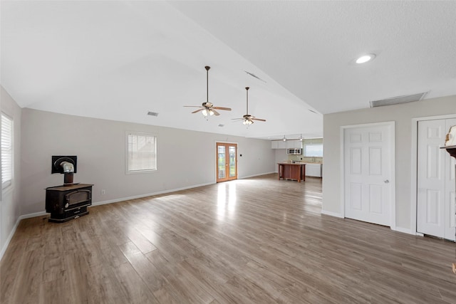 unfurnished living room featuring lofted ceiling, a wood stove, visible vents, a ceiling fan, and wood finished floors