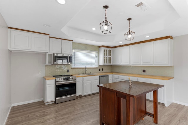 kitchen with light wood-style flooring, appliances with stainless steel finishes, white cabinetry, a sink, and a tray ceiling