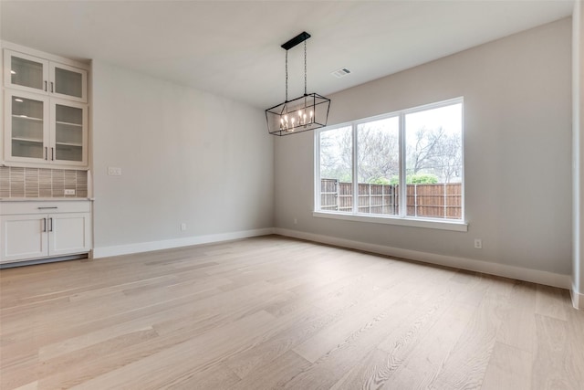 unfurnished dining area featuring baseboards, light wood-style floors, a chandelier, and visible vents