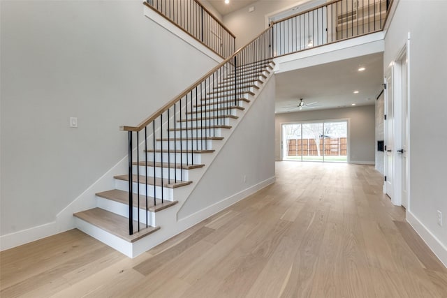 stairway featuring a ceiling fan, wood finished floors, baseboards, a towering ceiling, and recessed lighting