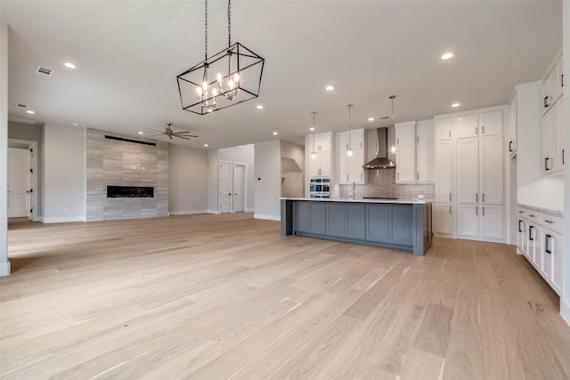 kitchen with white cabinets, tasteful backsplash, ceiling fan with notable chandelier, and wall chimney exhaust hood