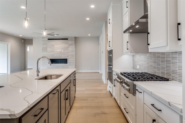 kitchen featuring recessed lighting, a sink, ceiling fan, wall chimney range hood, and appliances with stainless steel finishes