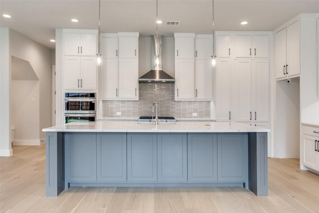 kitchen with stainless steel appliances, decorative backsplash, white cabinets, a kitchen island with sink, and wall chimney exhaust hood