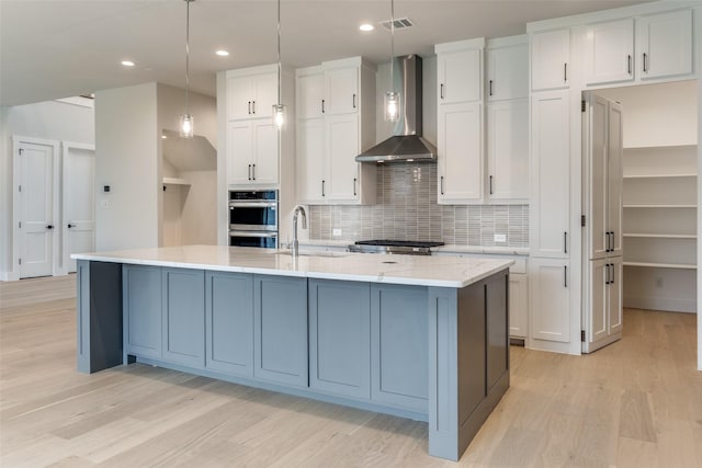 kitchen featuring wall chimney range hood, a sink, white cabinetry, and light wood-style floors