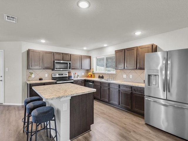 6348 Sloop St, Fort Worth, TX 76179 - kitchen featuring light countertops, a kitchen bar, a sink, light wood finished floors, and appliances with stainless steel finishes