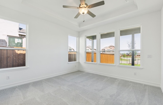 carpeted empty room featuring baseboards, a raised ceiling, ceiling fan, and plenty of natural light