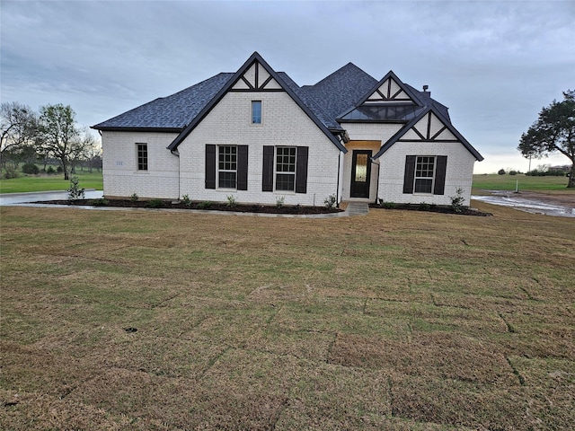 view of front of home featuring brick siding, roof with shingles, and a front lawn