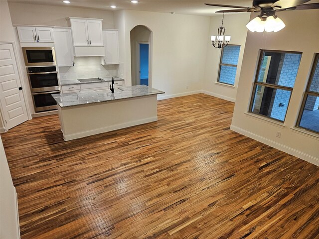 kitchen featuring wood finished floors, black electric stovetop, built in microwave, ceiling fan with notable chandelier, and arched walkways
