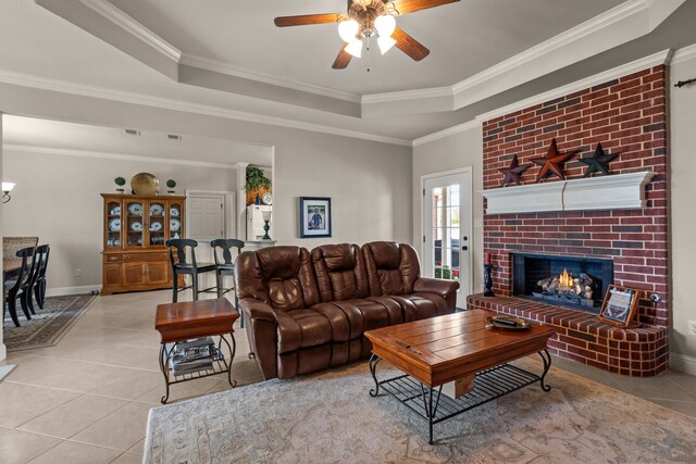 tiled living room with a brick fireplace, a ceiling fan, ornamental molding, and a raised ceiling