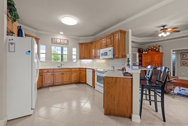 kitchen with a peninsula, white appliances, tasteful backsplash, a sink, and a kitchen breakfast bar
