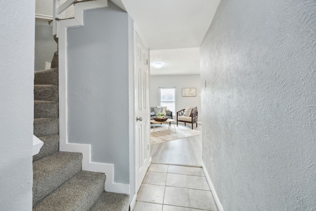 interior space featuring tile patterned floors, a textured wall, baseboards, and stairs