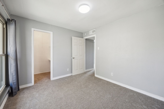 unfurnished bedroom featuring baseboards, carpet flooring, visible vents, and a walk in closet