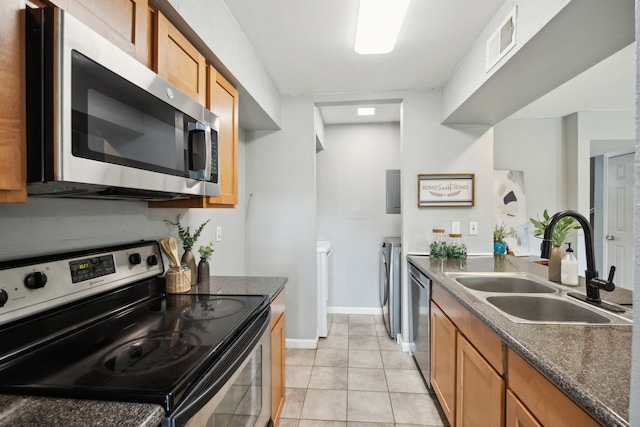 kitchen with washing machine and dryer, a sink, dark countertops, visible vents, and appliances with stainless steel finishes