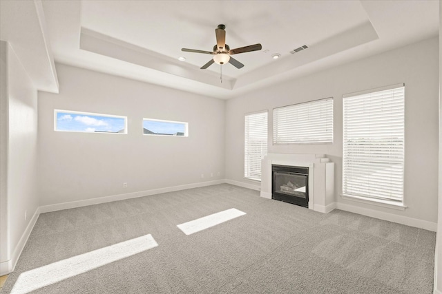 153 Whispering Winds Dr, Gunter, TX 75058 - unfurnished living room with a tray ceiling, carpet, a ceiling fan, a glass covered fireplace, and baseboards