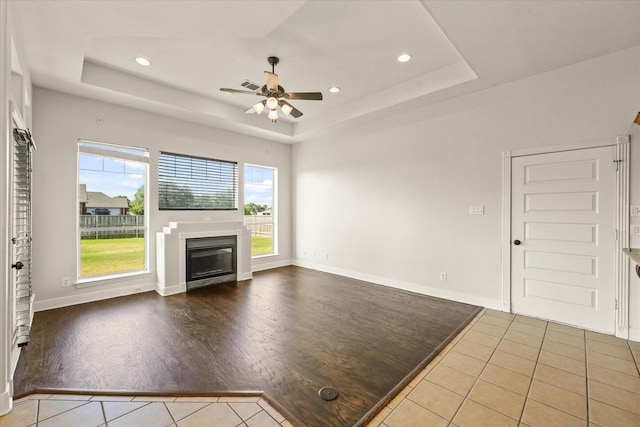 153 Whispering Winds Dr, Gunter, TX 75058 - unfurnished living room featuring tile patterned floors, a glass covered fireplace, a tray ceiling, ceiling fan, and recessed lighting