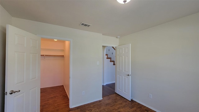 unfurnished bedroom with a closet, a walk in closet, dark wood-style floors, baseboards, and visible vents