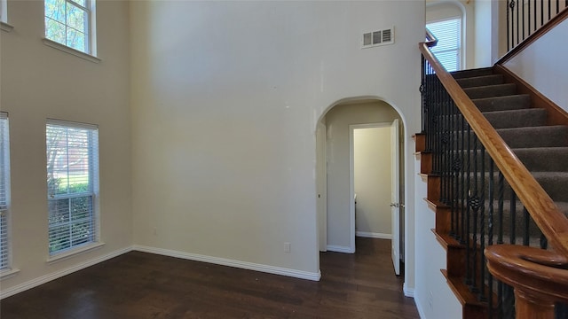 interior space with visible vents, wood finished floors, arched walkways, a wealth of natural light, and a high ceiling