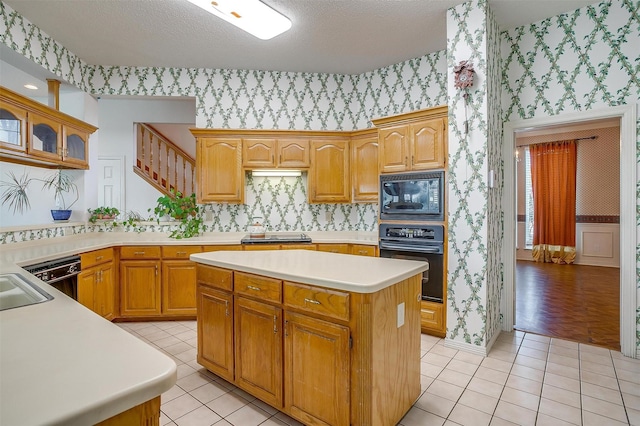 1002 Loch Lomond Dr, Arlington, TX 76012 - kitchen featuring light countertops, wallpapered walls, a kitchen island, light tile patterned flooring, and black appliances