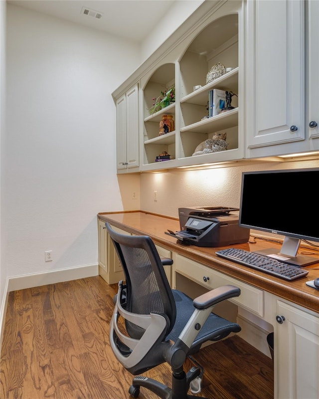 office area featuring wood finished floors, visible vents, built in desk, and baseboards
