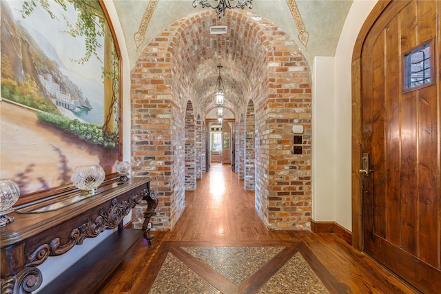 hall featuring wood-type flooring, arched walkways, vaulted ceiling, and brick wall