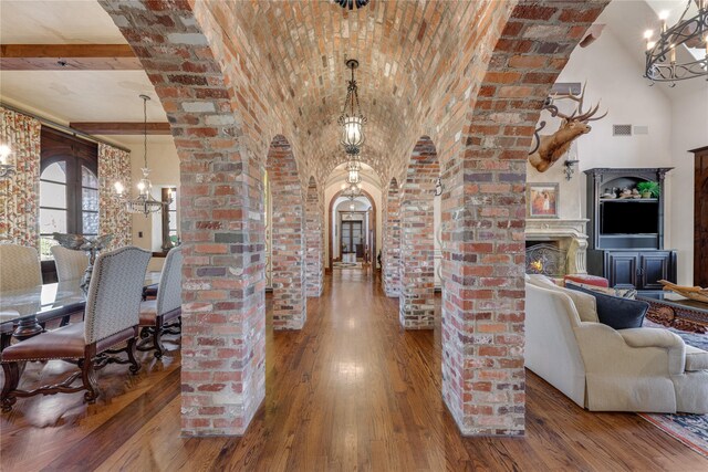 hall featuring arched walkways, an inviting chandelier, hardwood / wood-style floors, brick ceiling, and visible vents