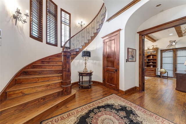 stairway featuring arched walkways, wood finished floors, and baseboards