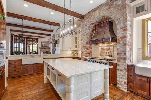 kitchen with a center island, custom exhaust hood, tasteful backsplash, a sink, and a peninsula