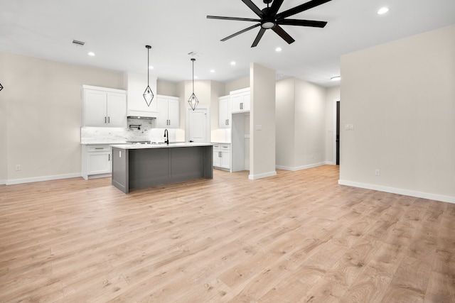 kitchen with light countertops, visible vents, white cabinets, ceiling fan, and a center island with sink