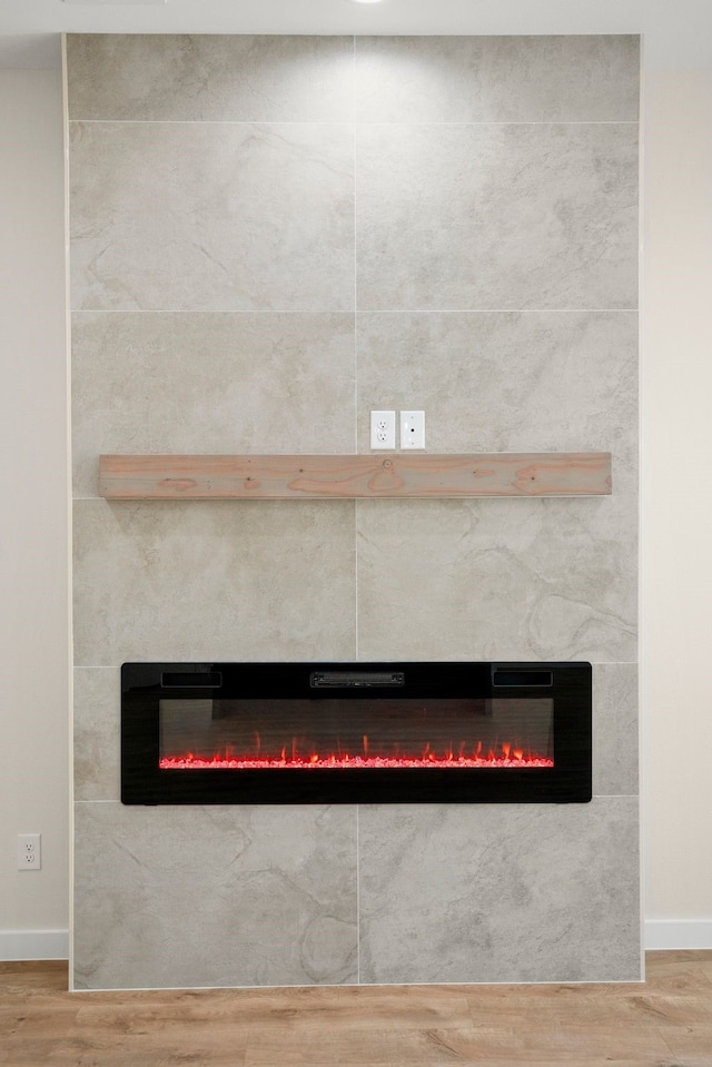 room details featuring a tiled fireplace, baseboards, and wood finished floors