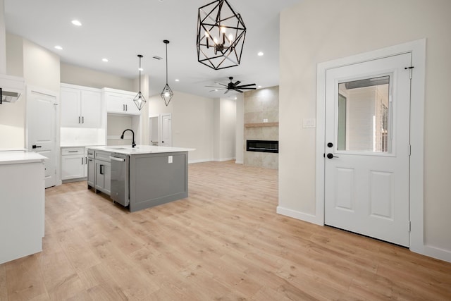 kitchen with light wood finished floors, a sink, a tiled fireplace, and dishwasher