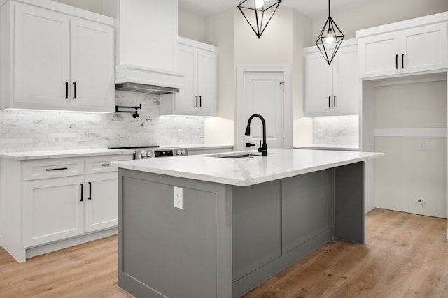 kitchen featuring a kitchen island with sink, white cabinetry, a sink, light wood-type flooring, and backsplash