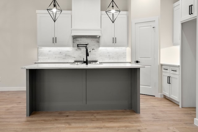 kitchen with an island with sink, light countertops, light wood finished floors, white cabinetry, and tasteful backsplash
