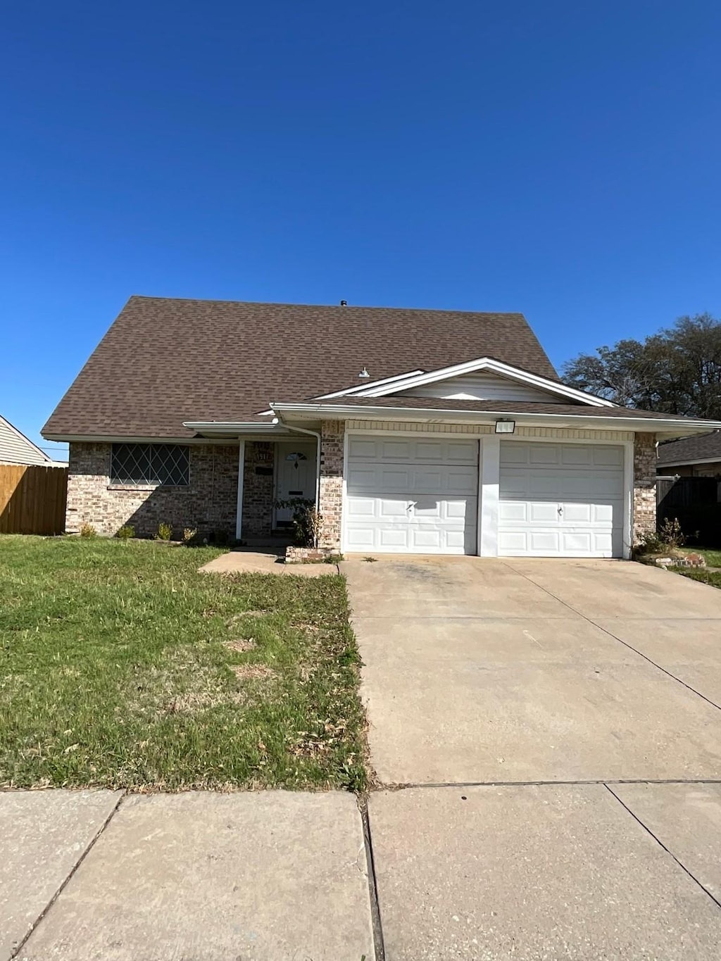 view of front of property featuring concrete driveway, fence, a front yard, brick siding, and a garage