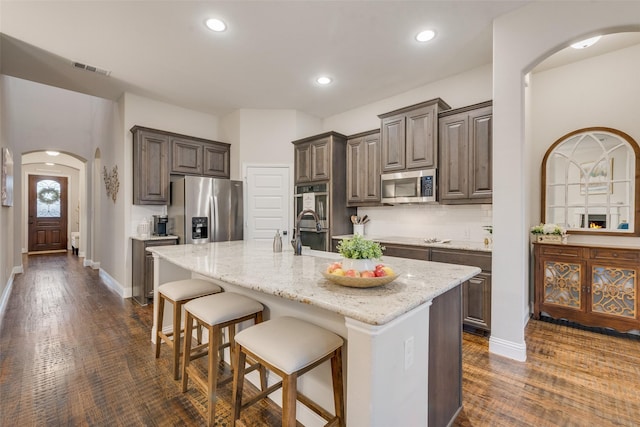 kitchen featuring a kitchen island with sink, a breakfast bar area, arched walkways, stainless steel appliances, and baseboards