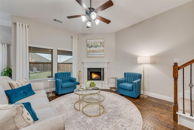 living room featuring stairs, ceiling fan, a lit fireplace, baseboards, and visible vents