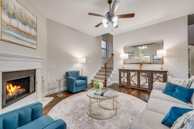 living area with stairway, wood finished floors, ceiling fan, a lit fireplace, and baseboards