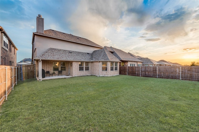 rear view of property featuring a fenced backyard, a chimney, brick siding, a lawn, and a patio