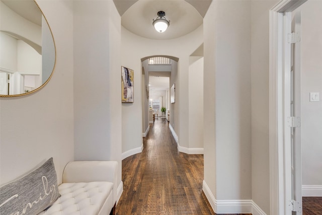 hall with arched walkways, wood finished floors, and baseboards