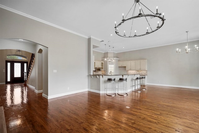 unfurnished living room featuring baseboards, wood finished floors, arched walkways, and an inviting chandelier