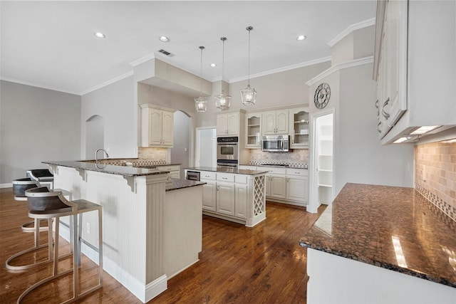 kitchen featuring a kitchen bar, a peninsula, dark wood finished floors, stainless steel microwave, and visible vents